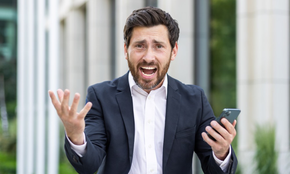 Hombre enfadado con su celular en la mano – Cómo bloquear mensajes de texto molestos en tu teléfono.