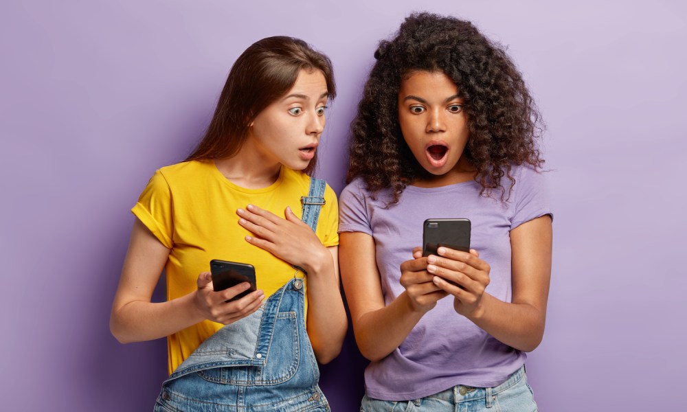 Dos mujeres jóvenes sorprendidas viendo sus celulares – Cómo ocultar fotos y videos en un teléfono Android.