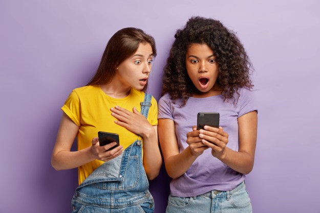 Dos mujeres jóvenes sorprendidas viendo sus celulares – Cómo ocultar fotos y videos en un teléfono Android.