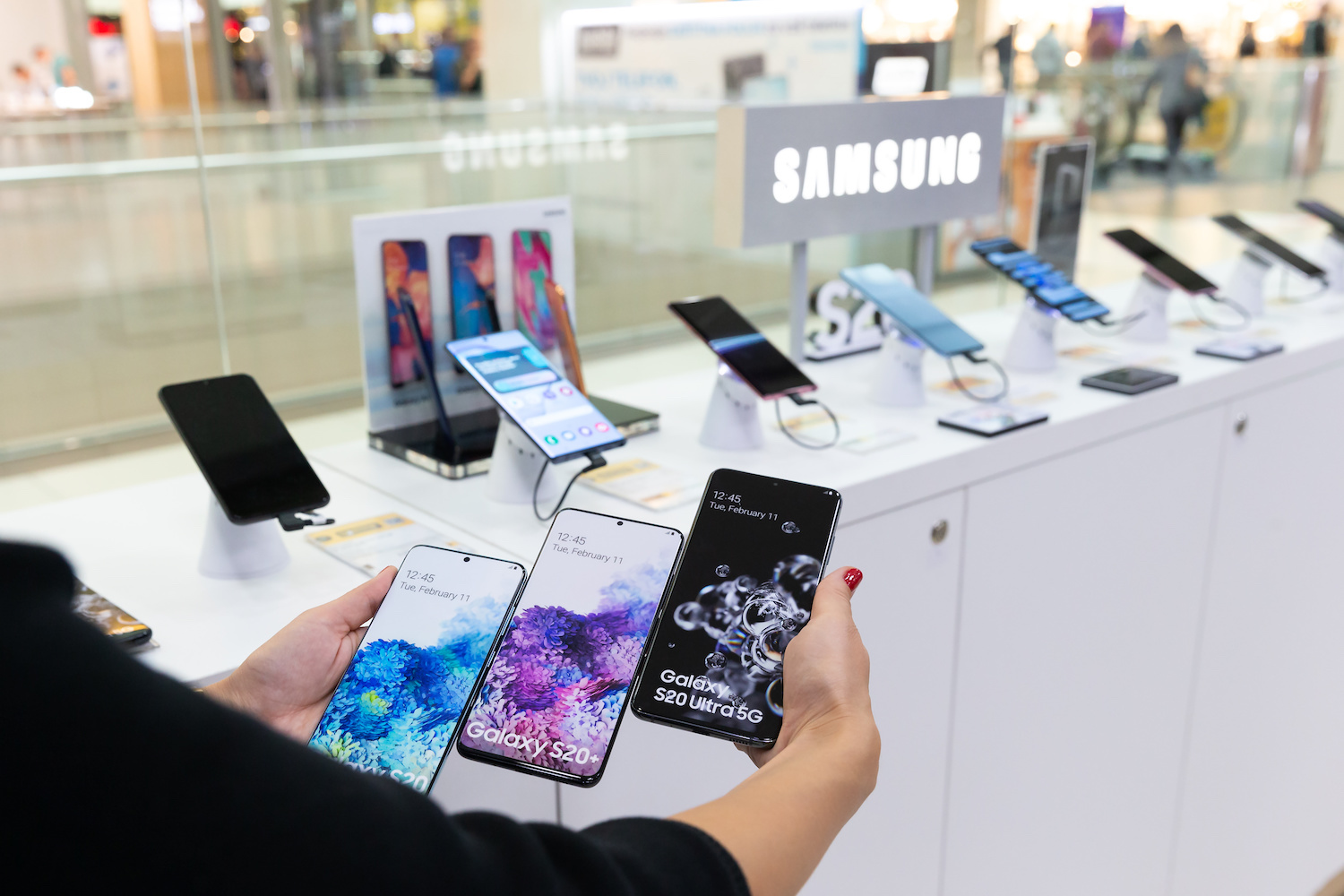 Persona mostrando tres teléfonos Samsung en una tienda – Estas son las diferencias entre los celulares Samsung Galaxy S, A, J y M.