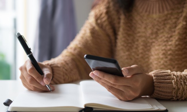 Una persona tomando nota en un cuaderno junto a su celular.