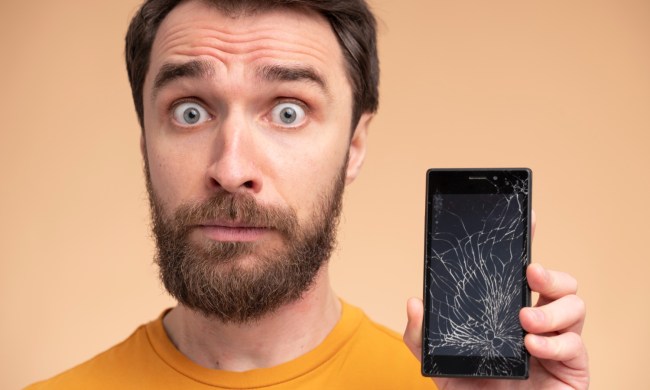 Retrato de un joven sorprendido mostrando su teléfono inteligente roto.