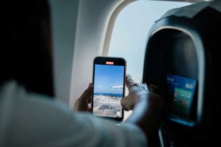 Una persona grabando un video con su celular por la ventana del avión.