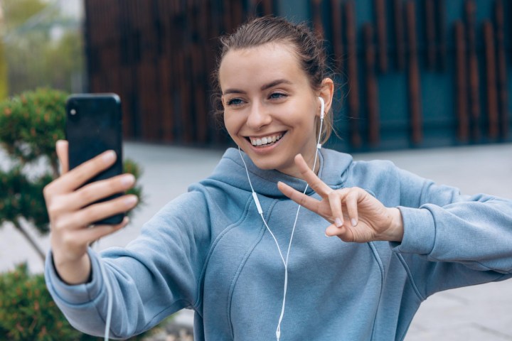 Una mujer con un celular y audífonos con cable sonriendo.